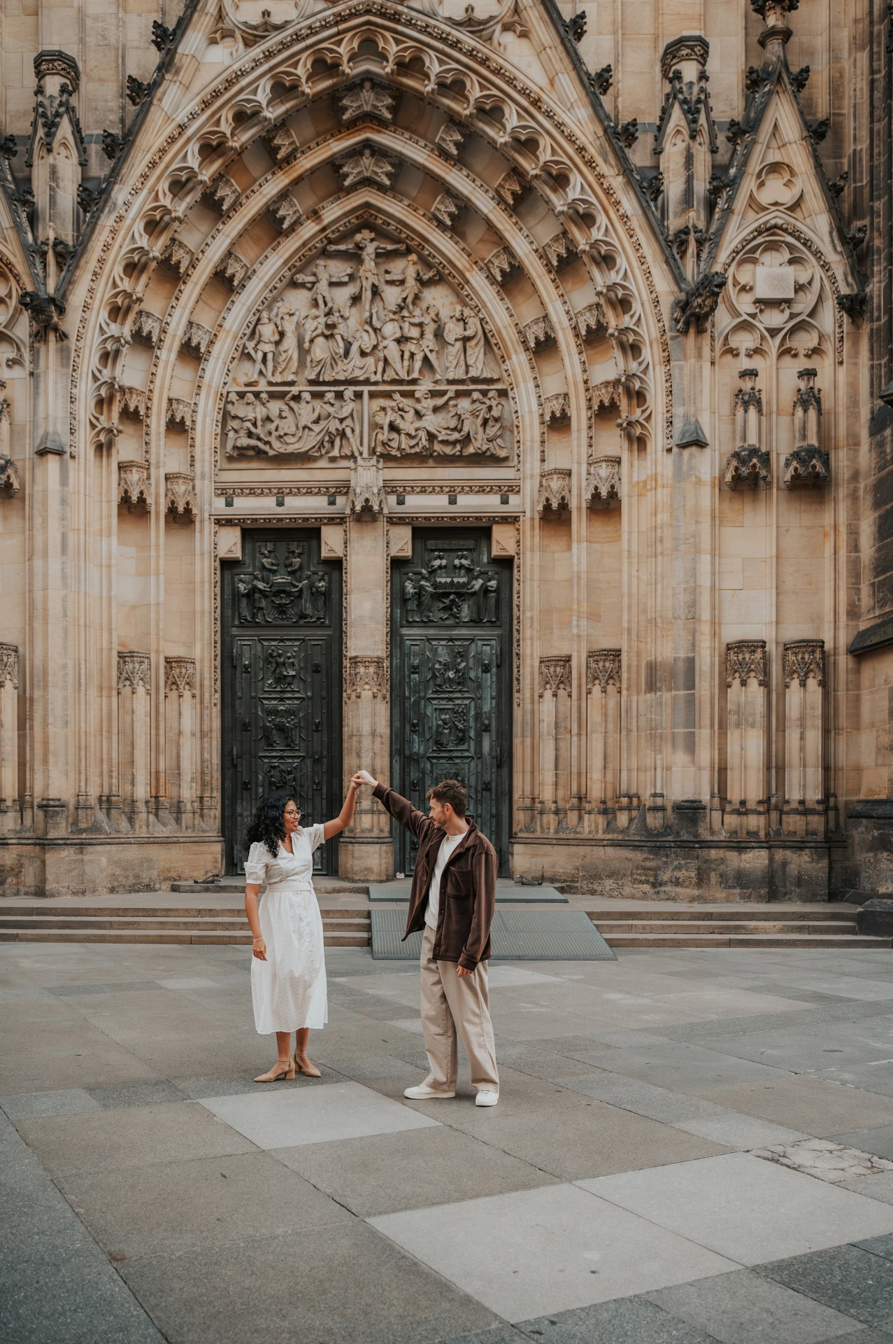 Couple walking away from the cathedral entrance together during an anniversary couple photoshoot in Prague.