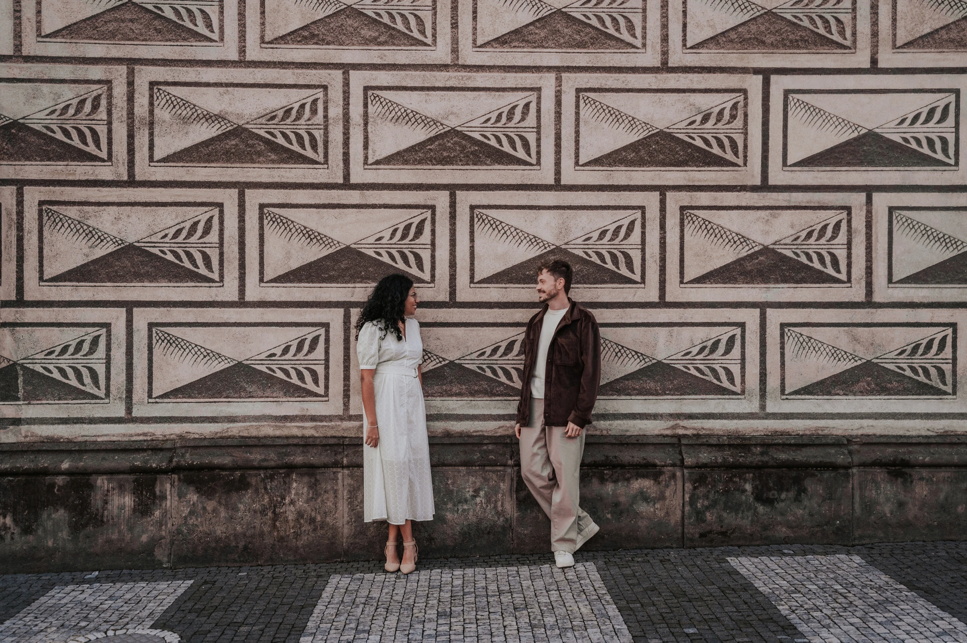 Wide portrait of the couple beside the patterned castle-area facade during an anniversary couple photoshoot in Prague.