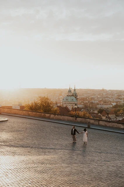Prague anniversary photoshoot: wide portrait of the couple on the sunlit cobbled square. Wide portrait of the couple on the sunlit cobbled square during an anniversary couple photoshoot in Prague.