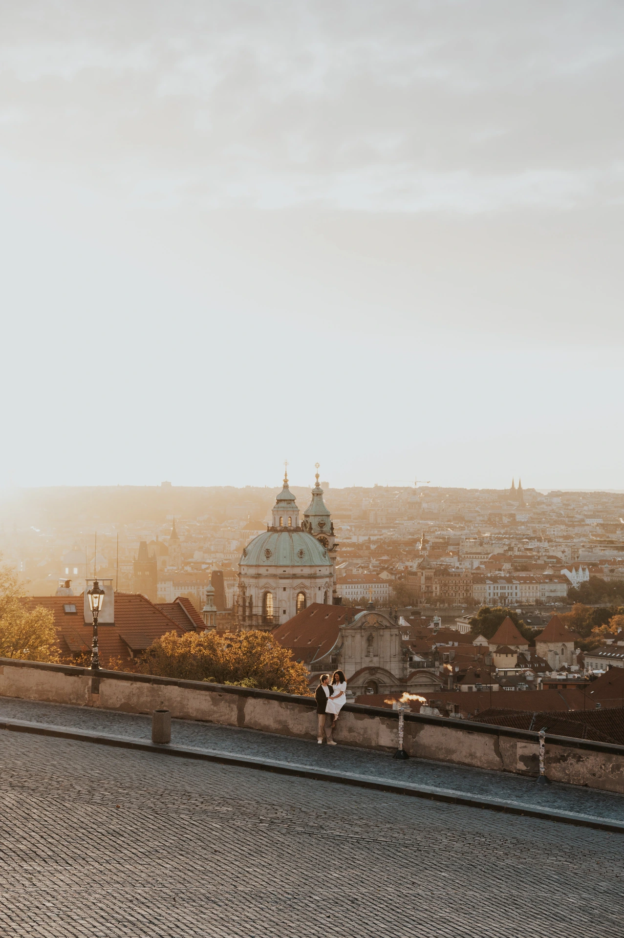 Wide view of the couple and the city below at sunrise during an anniversary couple photoshoot in Prague.