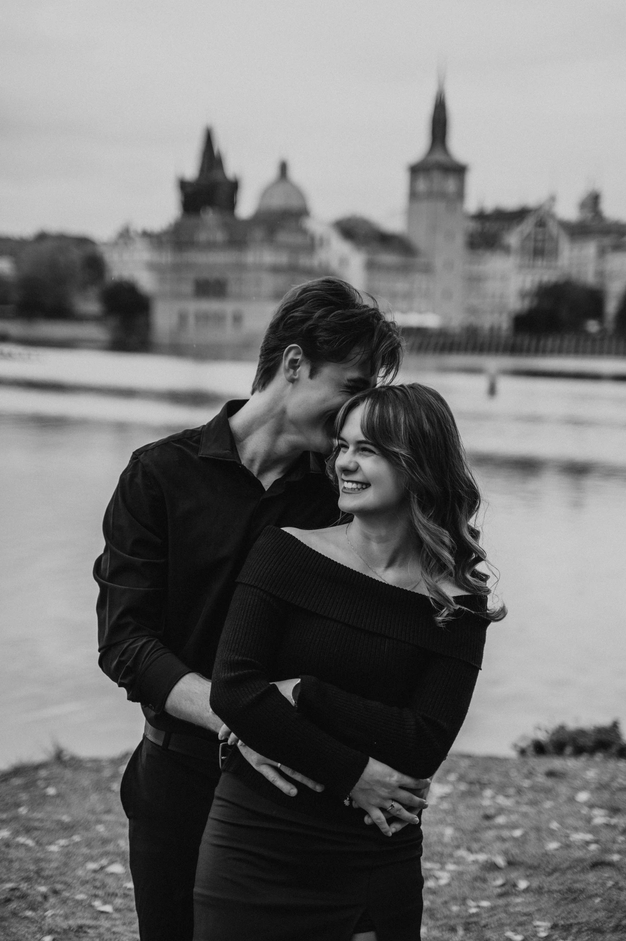 Black and white portrait of the couple cuddling by the river during a couple photoshoot in Prague.