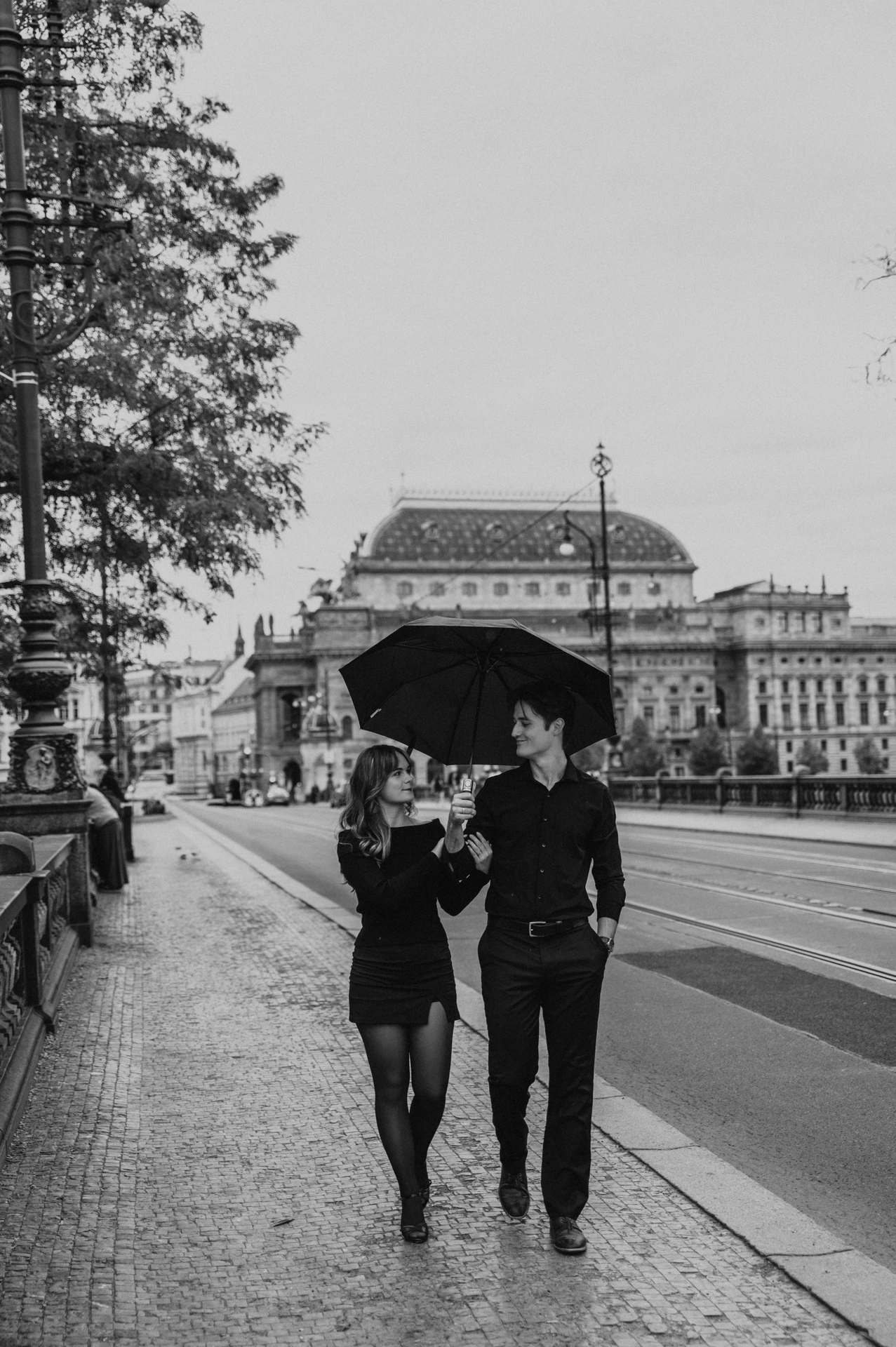 Black and white portrait of the couple walking under an umbrella during a couple photoshoot in Prague.