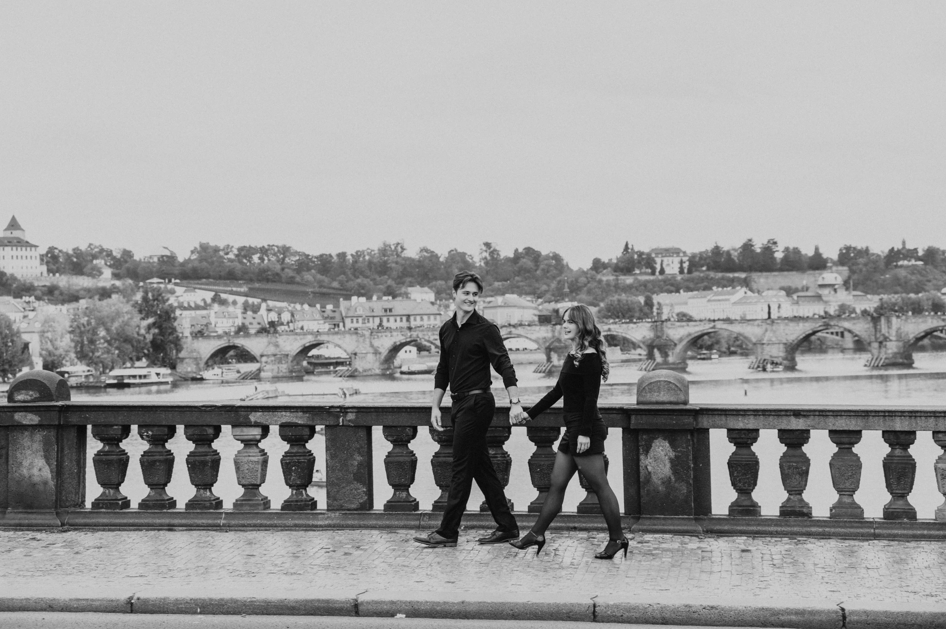 Black and white walk beside the bridge balustrade during a couple photoshoot in Prague.