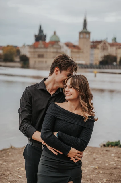 Couple cuddling with the city across the Vltava during a couple photoshoot in Prague.