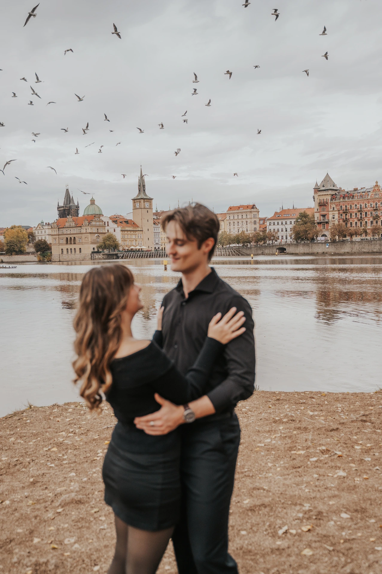 Couple embracing as birds fly above the river during a couple photoshoot in Prague.