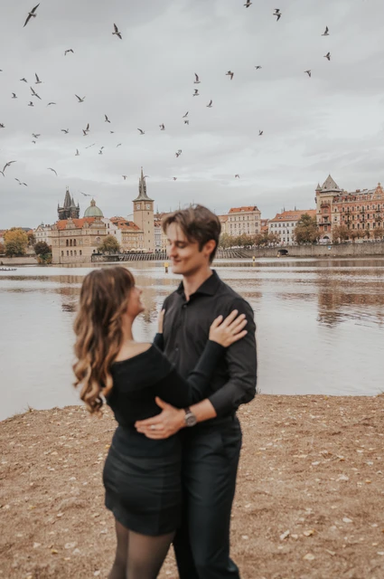 Prague couple photoshoot: couple embracing as birds fly above the river. Couple embracing as birds fly above the river during a couple photoshoot in Prague.