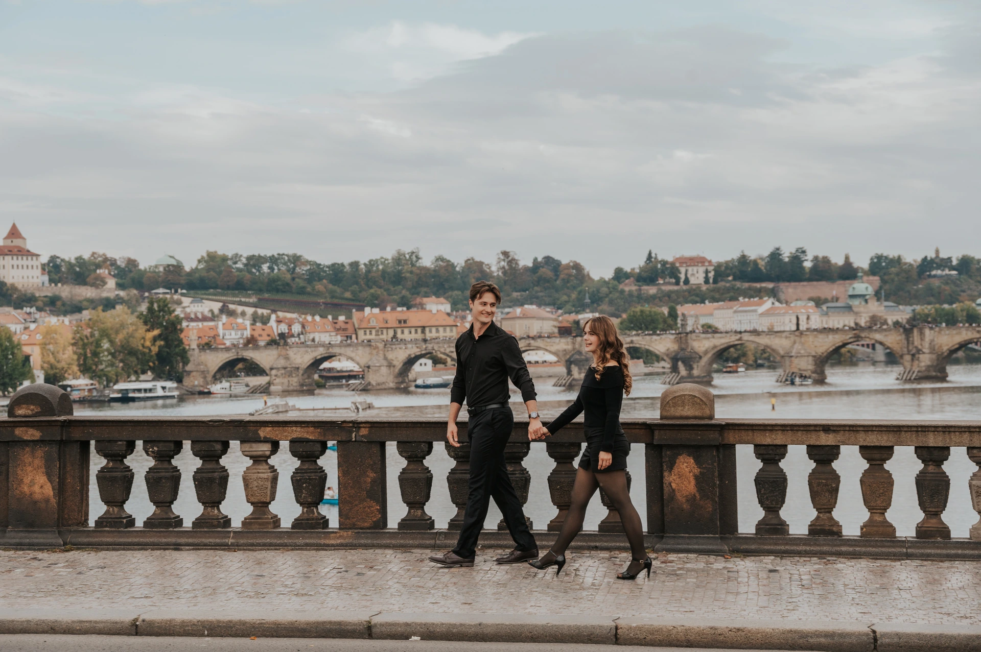 Prague couple photoshoot: couple holding hands as they walk across Legion Bridge. Couple holding hands as they walk across Legion Bridge during a couple photoshoot in Prague.