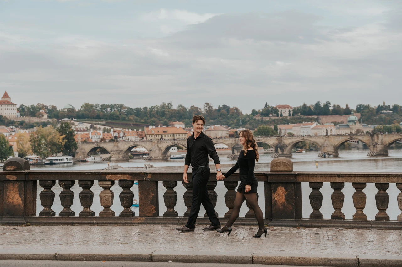 Prague couple photoshoot: couple holding hands as they walk across Legion Bridge. Couple holding hands as they walk across Legion Bridge during a couple photoshoot in Prague.