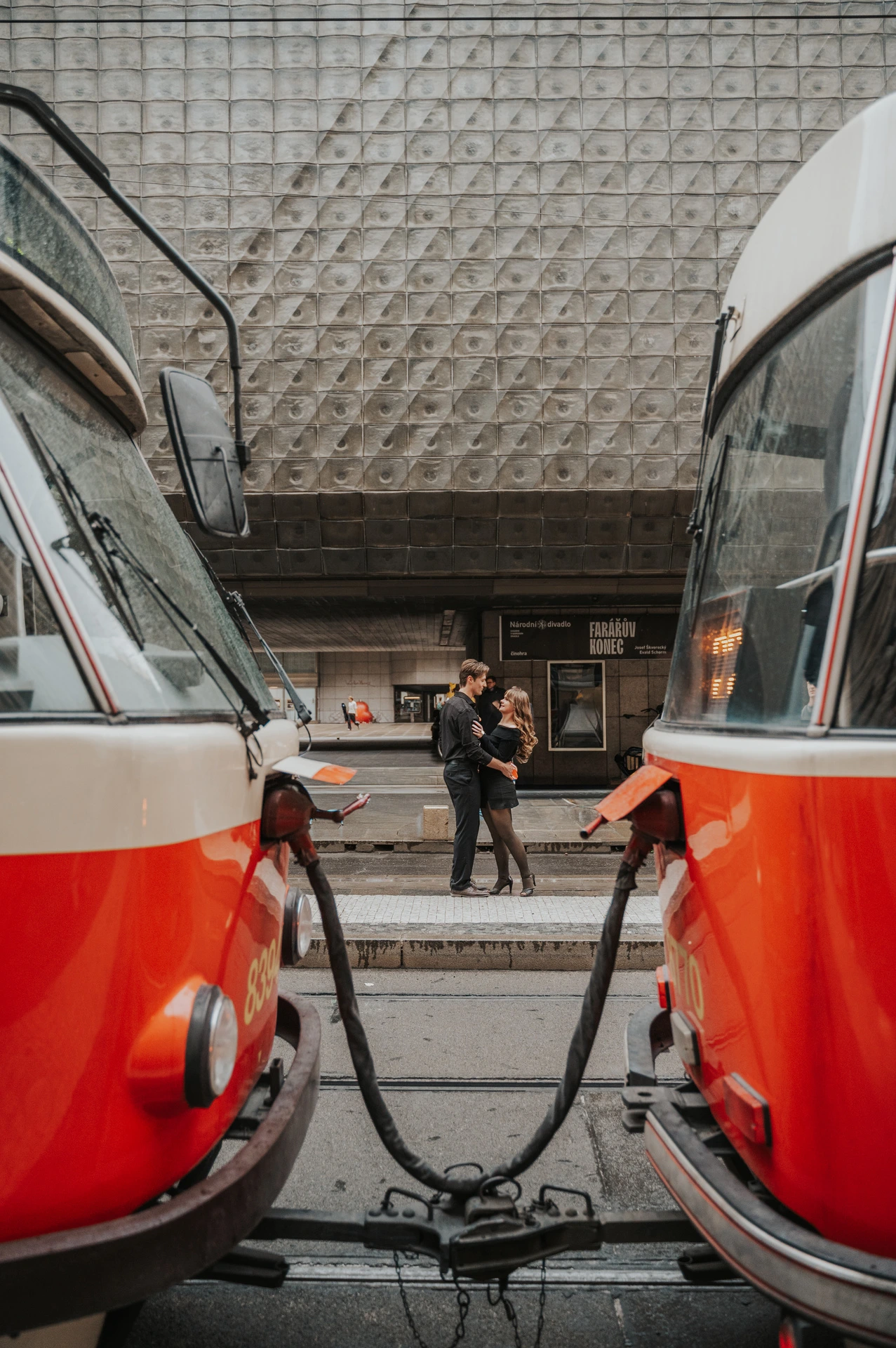 Couple holding hands between two red Prague trams during a couple photoshoot in Prague.