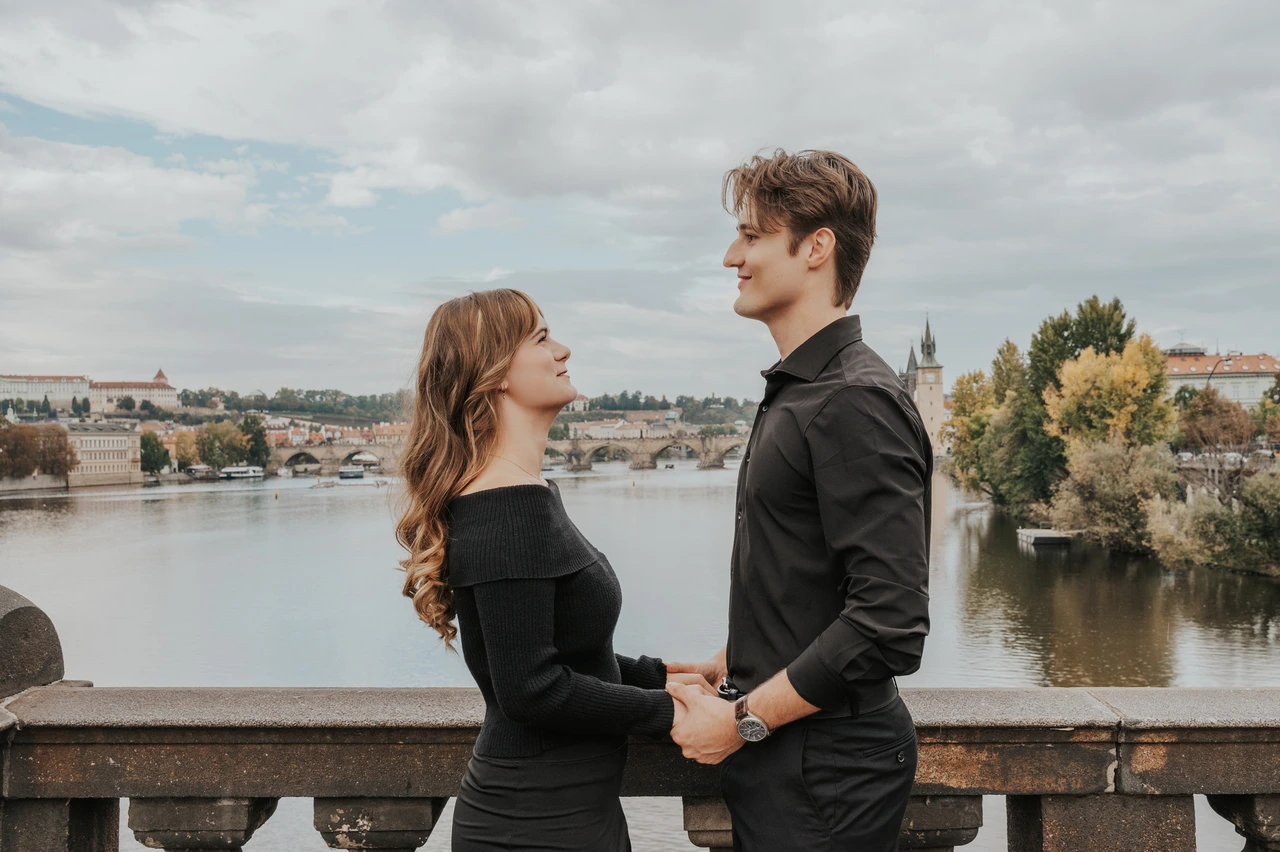 Prague couple photoshoot: couple holding hands with the Vltava behind them. Couple holding hands with the Vltava behind them during a couple photoshoot in Prague.