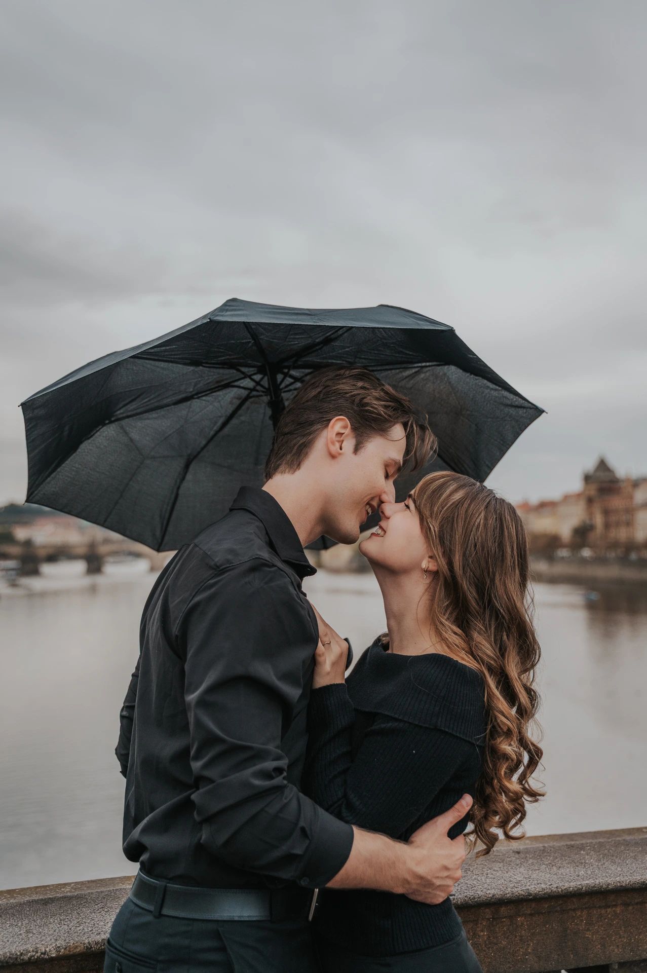 Couple kissing beneath their umbrella on the bridge during a couple photoshoot in Prague.