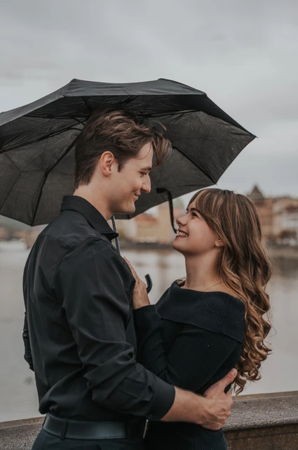 Couple looking at each other beneath a black umbrella during a couple photoshoot in Prague.
