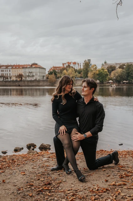Prague couple photoshoot: couple sharing a playful moment on the leaf-covered riverbank. Couple sharing a playful moment on the leaf-covered riverbank during a couple photoshoot in Prague.