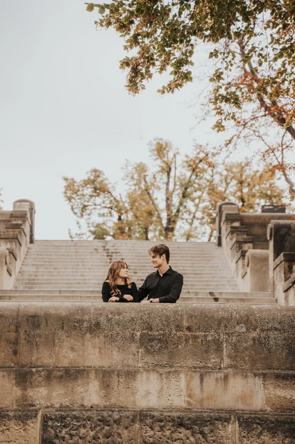 Prague couple photoshoot: couple sitting close behind a stone riverside wall. Couple sitting close behind a stone riverside wall during a couple photoshoot in Prague.