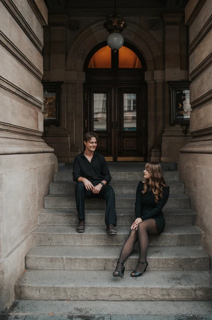 Prague couple photoshoot: couple sitting on the steps beneath an arched theatre door. Couple sitting on the steps beneath an arched theatre door during a couple photoshoot in Prague.