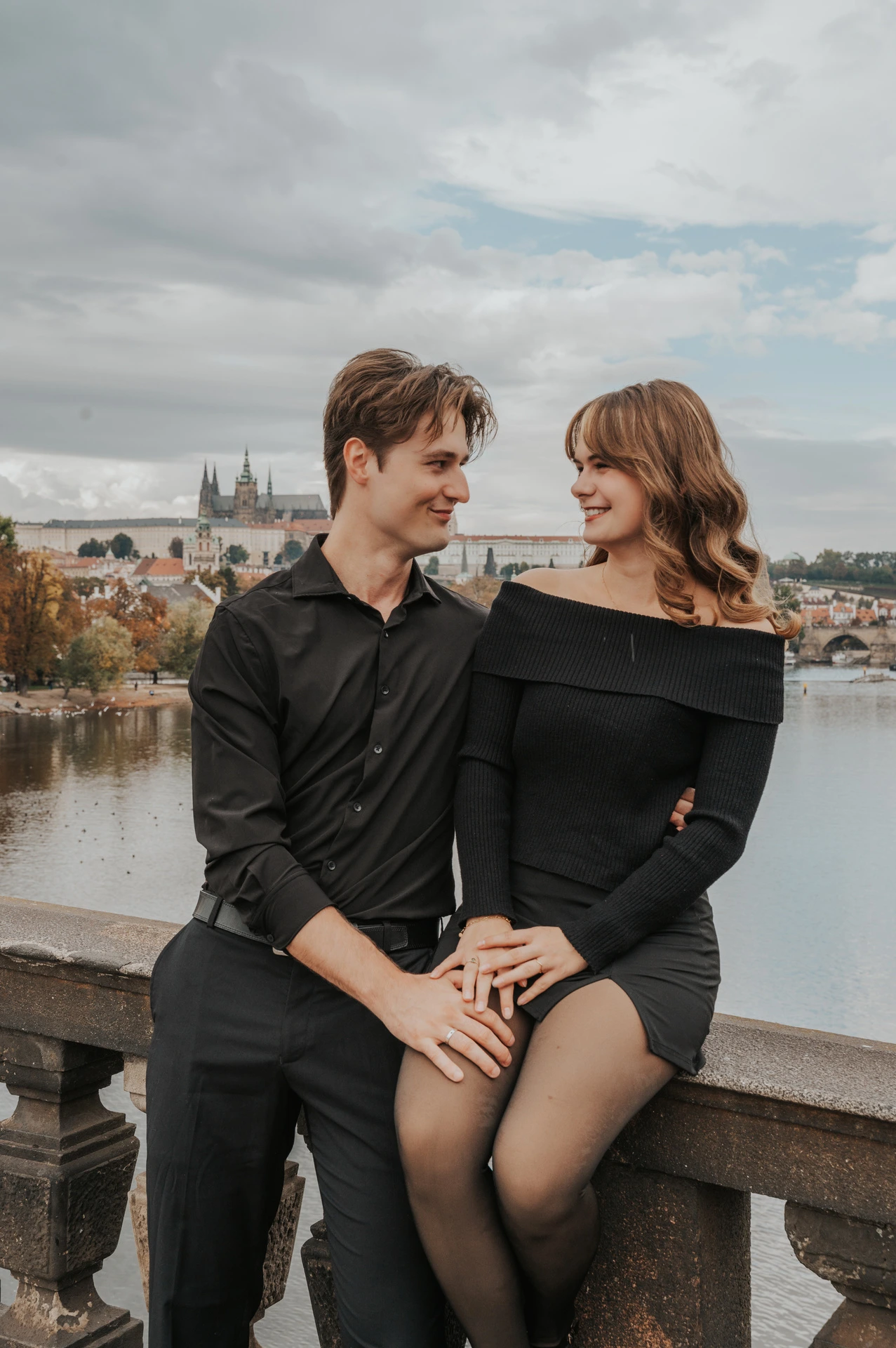 Couple sitting together on the Legion Bridge railing during a couple photoshoot in Prague.
