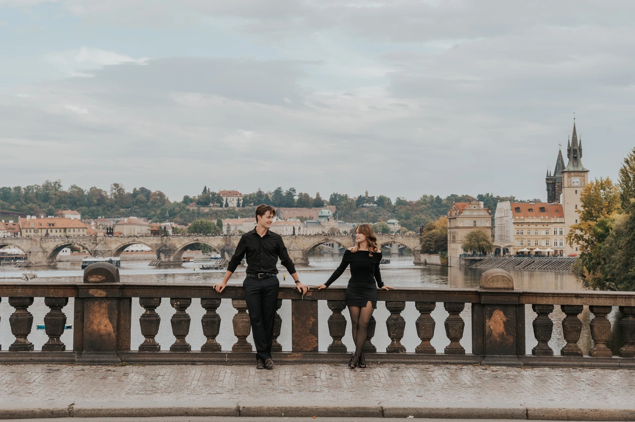 Prague couple photoshoot: couple smiling while leaning on the bridge balustrade. Couple smiling while leaning on the bridge balustrade during a couple photoshoot in Prague.