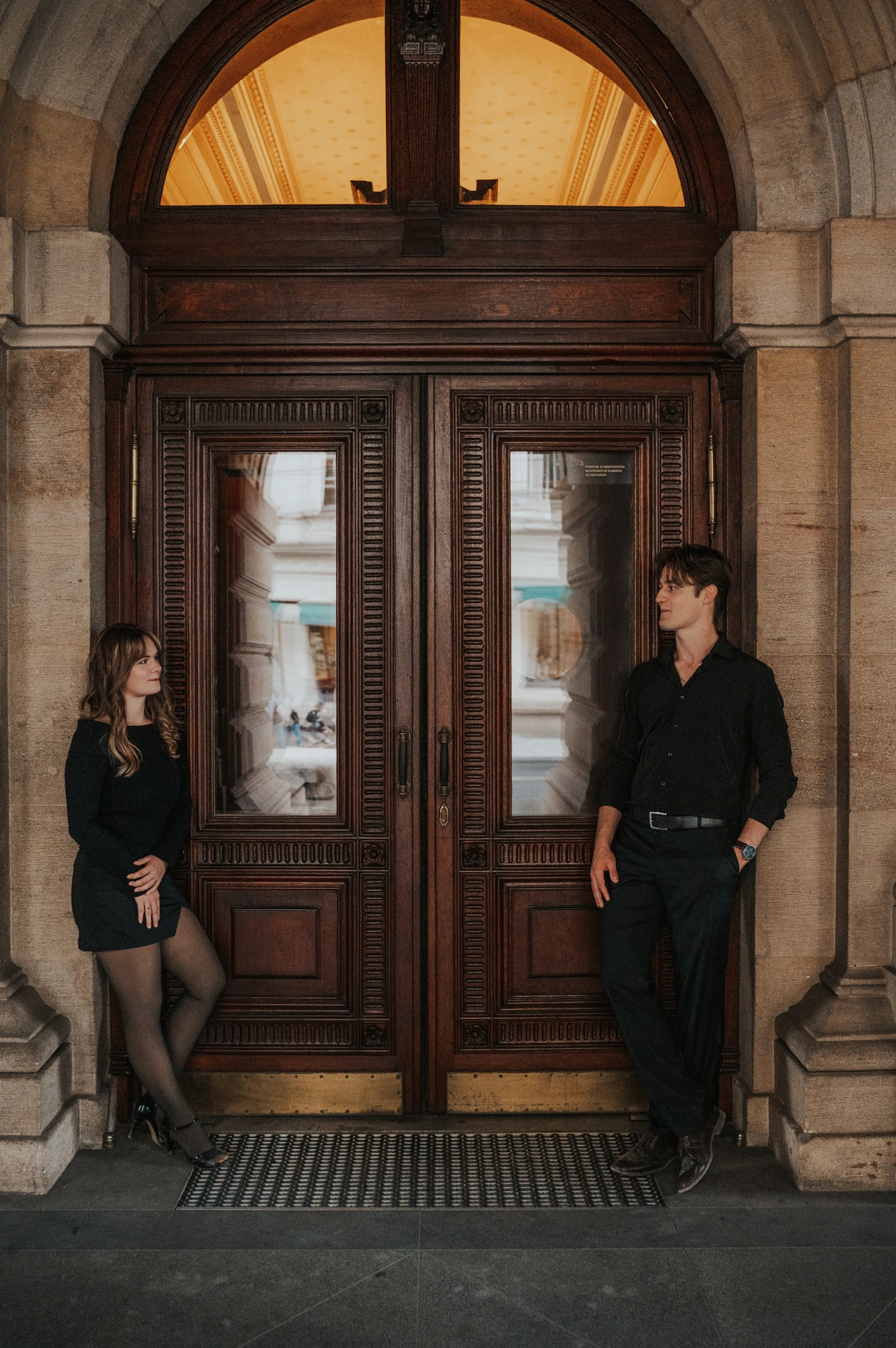 Couple standing either side of a wooden theatre door during a couple photoshoot in Prague.
