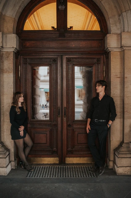 Prague couple photoshoot: couple standing either side of a wooden theatre door. Couple standing either side of a wooden theatre door during a couple photoshoot in Prague.