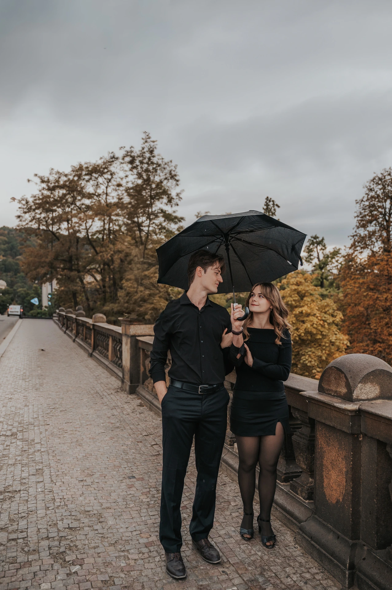 Couple walking past autumn trees on Legion Bridge during a couple photoshoot in Prague.