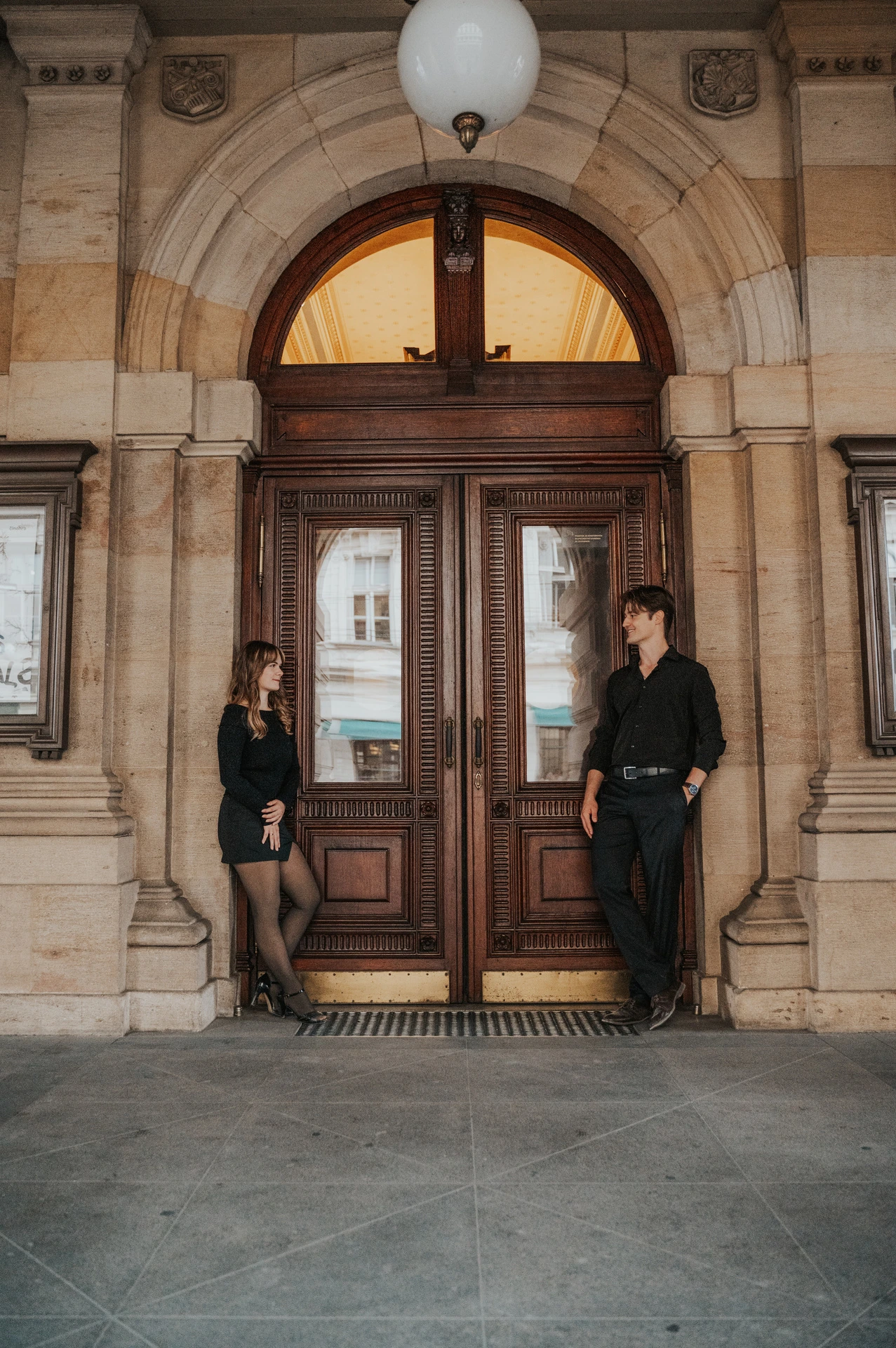 Wide portrait of the couple beneath the theatre arcade during a couple photoshoot in Prague.