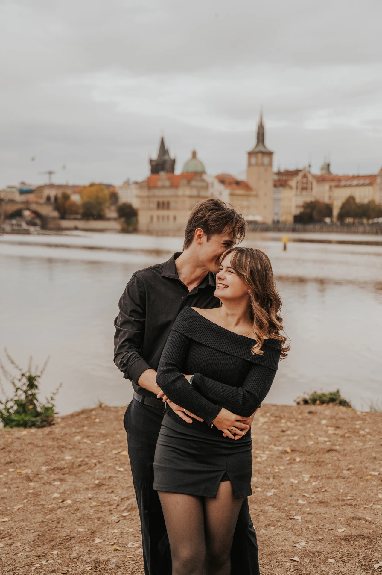 Wide portrait of the couple embracing beside the water during a couple photoshoot in Prague.
