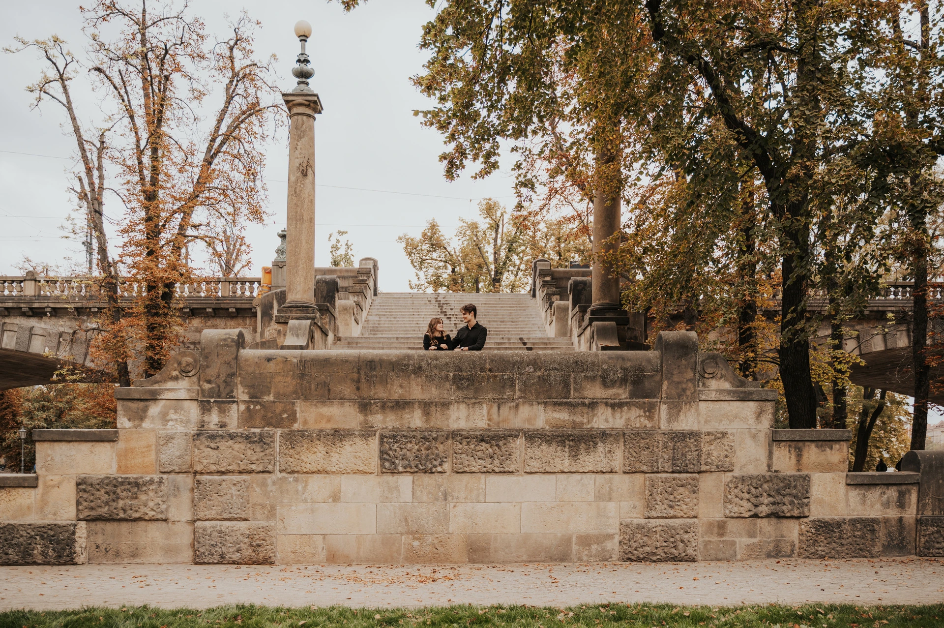 Wide view of the couple sitting on the stone island steps during a couple photoshoot in Prague.