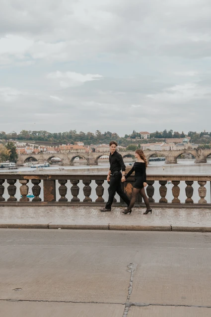 Prague couple photoshoot: wide view of the couple walking along the Legion Bridge balustrade. Wide view of the couple walking along the Legion Bridge balustrade during a couple photoshoot in Prague.