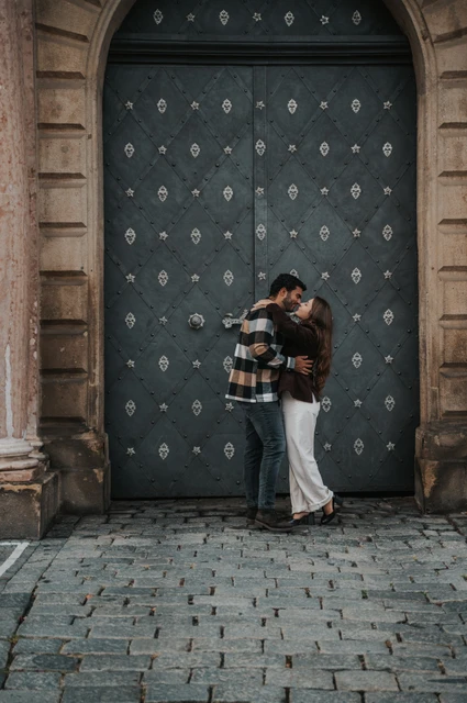 Prague couple photoshoot: an embrace at the dark studded gateway Couple embracing in front of a tall dark gateway decorated with metal studs during their Prague couple photoshoot.