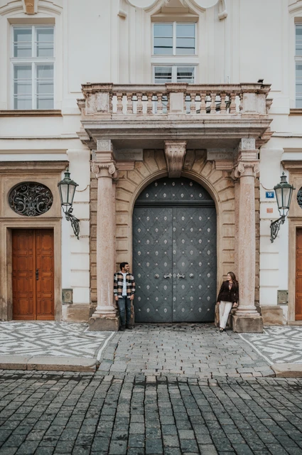 Prague couple photoshoot: a portrait at the tall arched castle gateway Couple standing on either side of a tall arched gateway framed by carved stonework during their Prague couple photoshoot.