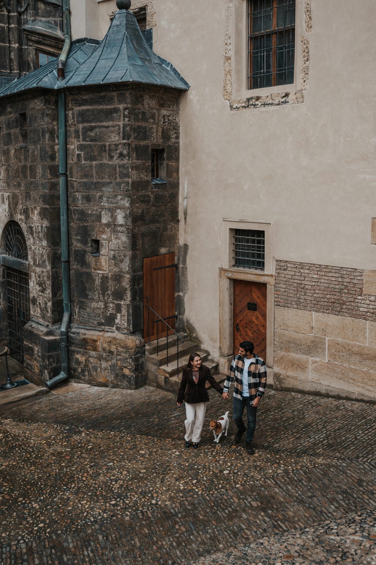 High-angle photograph of the couple and their dog beside the cathedral in a narrow castle lane during their Prague couple photoshoot.