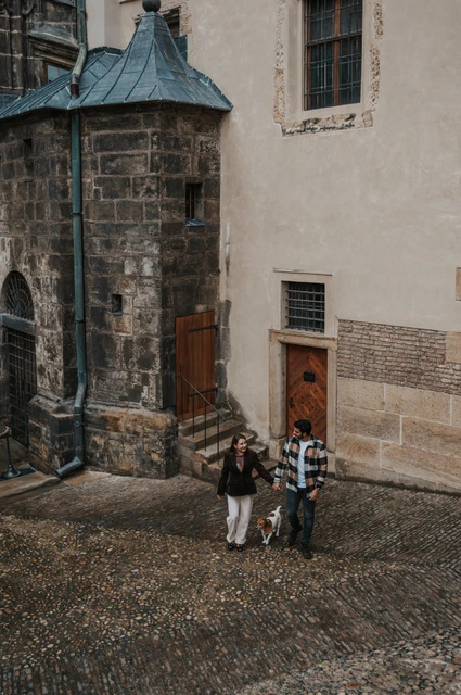 Prague couple photoshoot: a view down into the castle lane High-angle photograph of the couple and their dog beside the cathedral in a narrow castle lane during their Prague couple photoshoot.