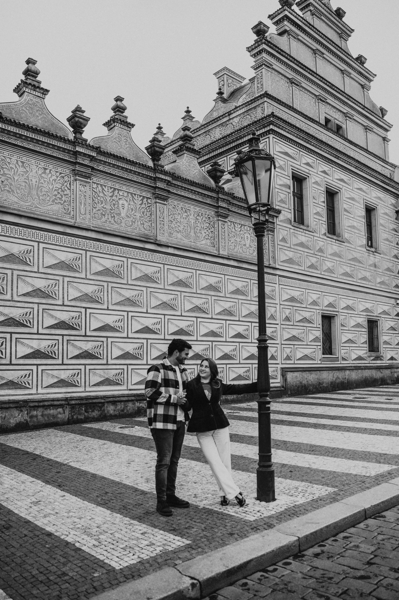 Black-and-white photograph of the couple holding hands beside a lamppost in the castle district during their Prague couple photoshoot.