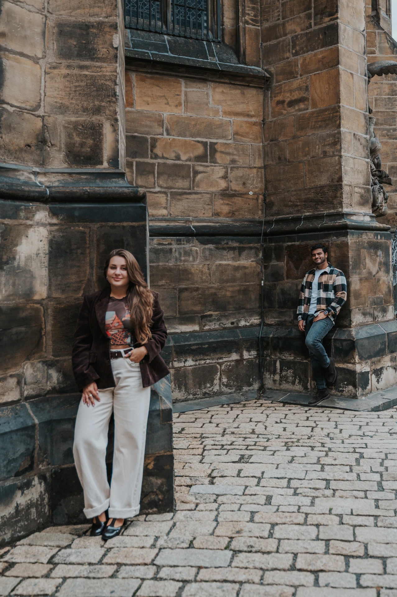Woman holding Amigo beside a cathedral corner while her partner stands a little behind during their Prague couple photoshoot.