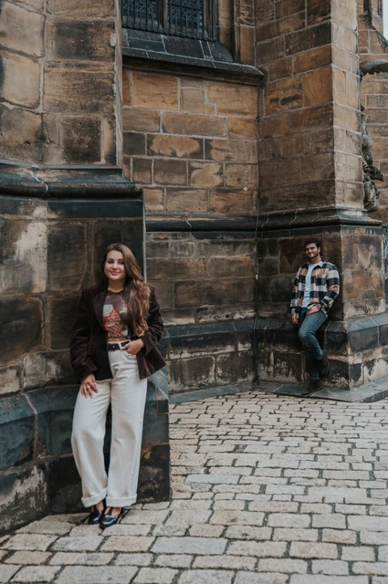 Prague couple photoshoot: amigo and the couple by a cathedral corner Woman holding Amigo beside a cathedral corner while her partner stands a little behind during their Prague couple photoshoot.