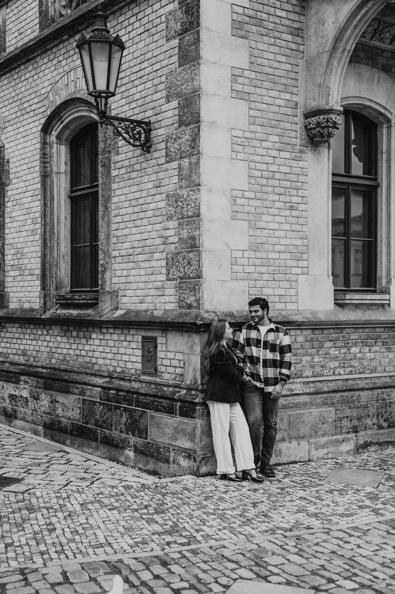 Black-and-white portrait of the couple together beside a stone cathedral corner and lantern during their Prague couple photoshoot.