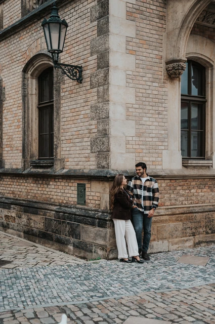 Couple leaning close beside a stone cathedral corner with a wall-mounted lantern above during their Prague couple photoshoot.