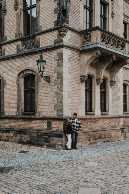 Prague couple photoshoot: a wide portrait at the cathedral corner Distant portrait of the couple together at a stone corner beneath tall cathedral windows during their Prague couple photoshoot.