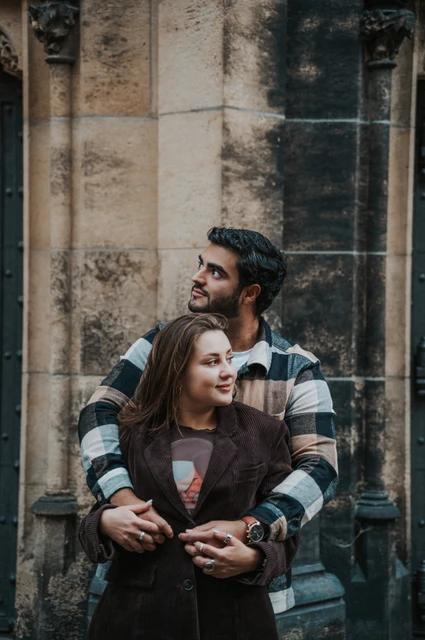 Prague couple photoshoot: looking up together outside the cathedral Couple looking upwards as they stand close together in front of the cathedral's dark doors during their Prague couple photoshoot.