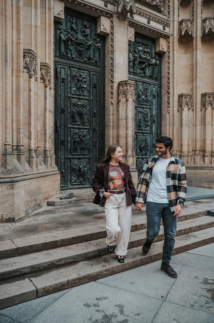 Prague couple photoshoot: walking down the cathedral steps with Amigo Couple walking down the cathedral steps while the woman carries their dog Amigo during their Prague couple photoshoot.