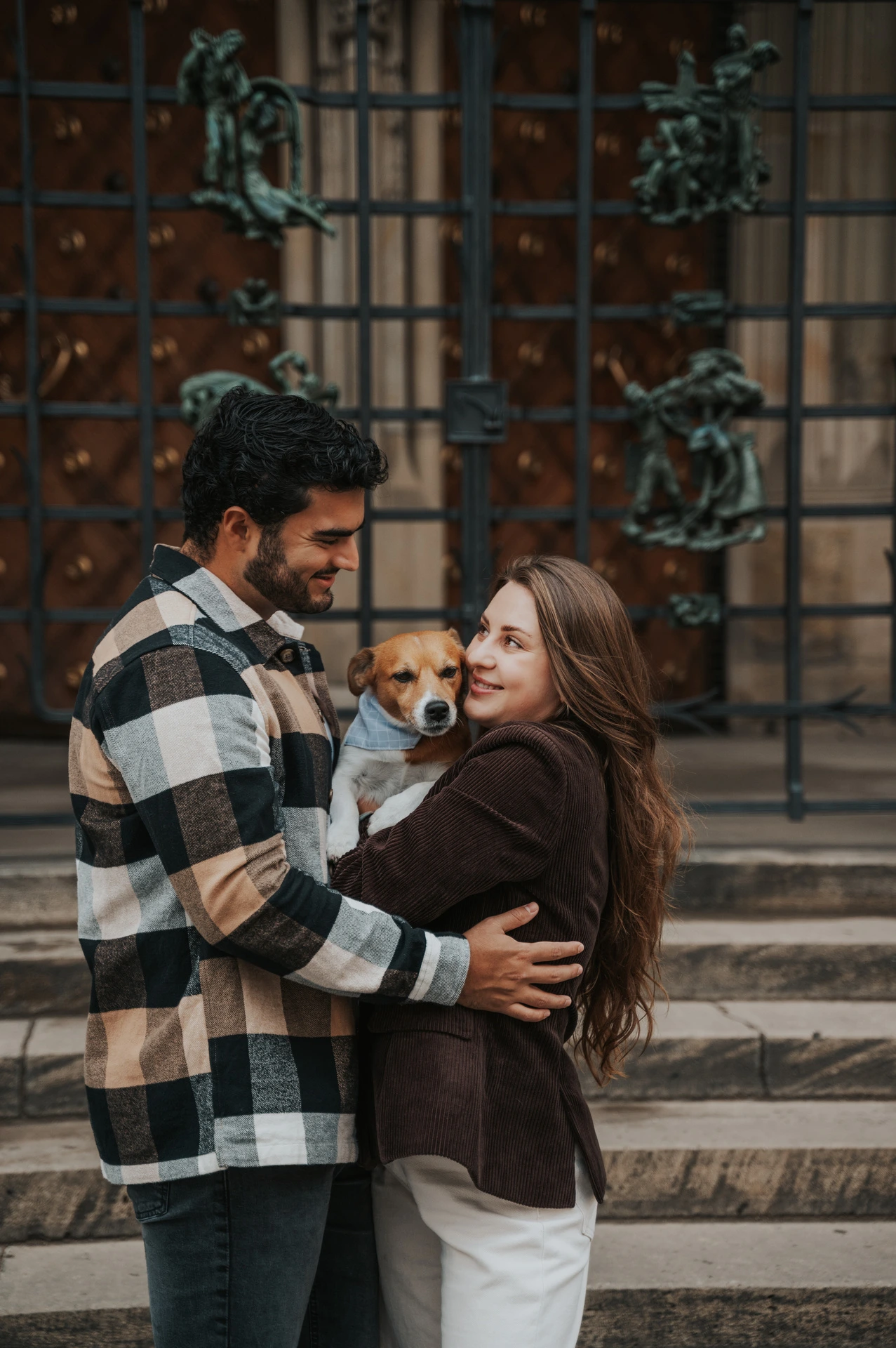 Couple smiling together while holding their dog Amigo outside the cathedral during their Prague couple photoshoot.
