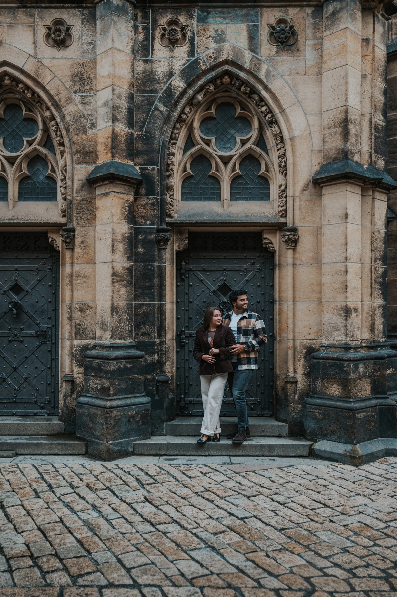 Couple holding Amigo in front of a pointed Gothic cathedral doorway during their Prague couple photoshoot.