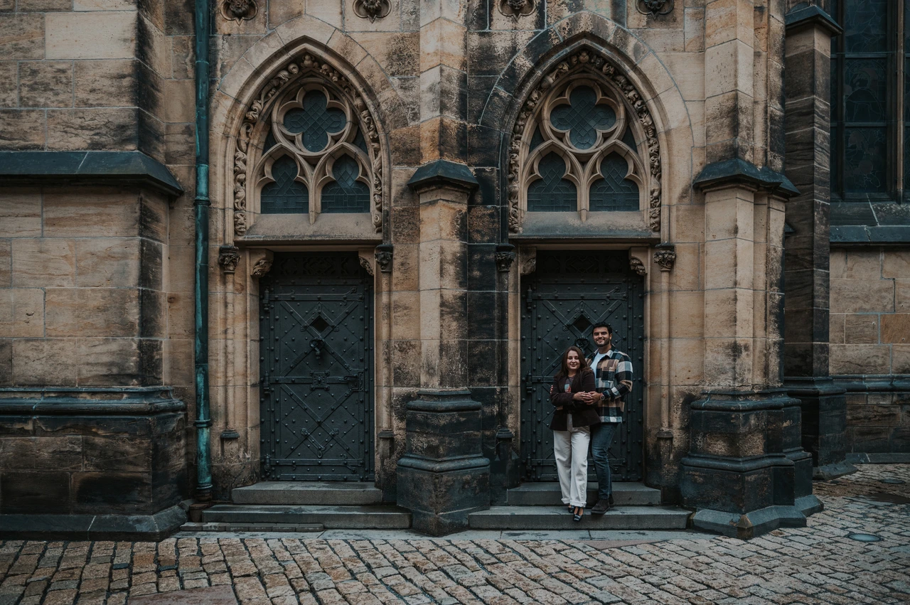 Prague couple photoshoot: with Amigo beneath the Gothic doorways Wide photograph of the couple with Amigo beneath pointed Gothic doorways at the cathedral during their Prague couple photoshoot.