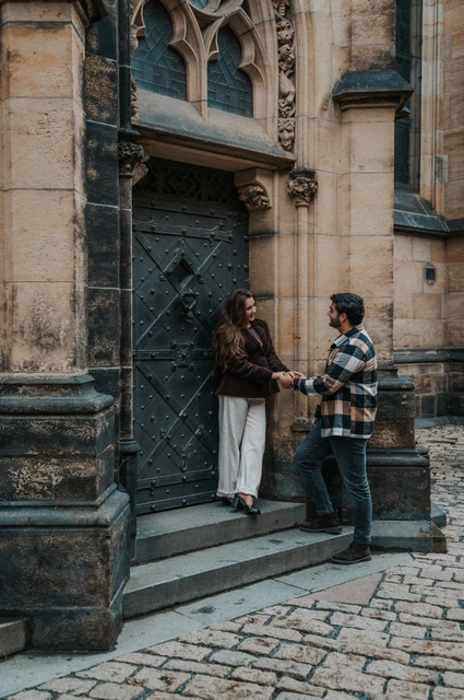 Prague couple photoshoot: holding hands with Amigo on the cathedral steps Couple holding hands on the cathedral steps with their small dog in the woman's arms during their Prague couple photoshoot.