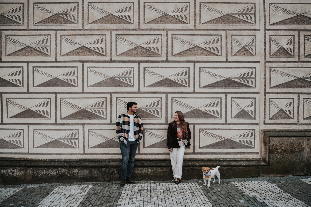 Prague couple photoshoot: with Amigo beside a patterned castle facade Couple standing apart beside a patterned stone facade, with their dog Amigo between them during their Prague couple photoshoot.