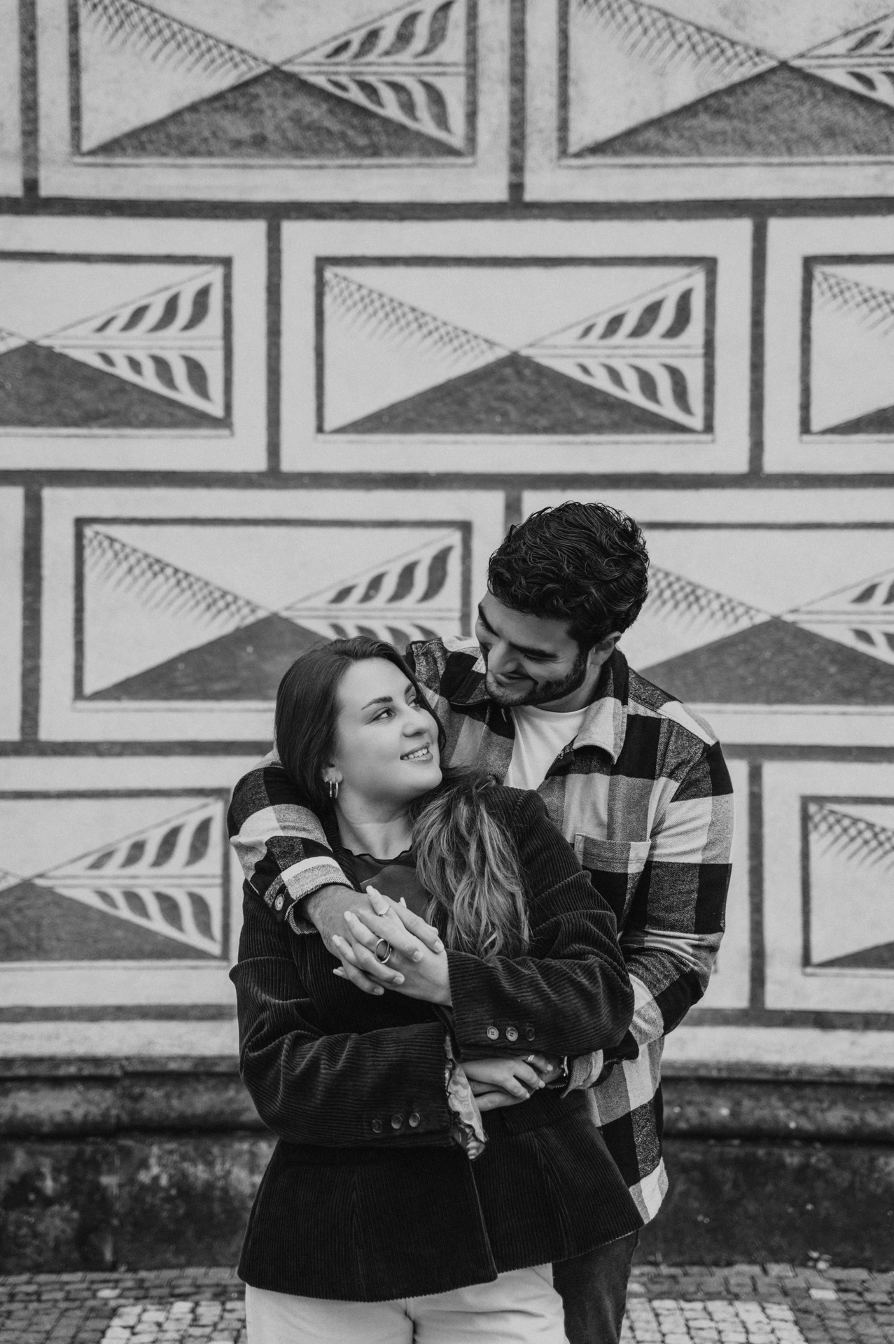 Black-and-white portrait of the couple embracing beside a patterned stone facade during their Prague couple photoshoot.