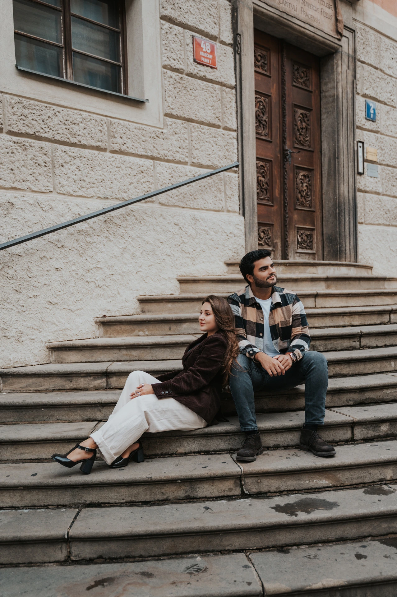 Woman leaning back beside her partner on stone steps while Amigo sits between them during their Prague couple photoshoot.