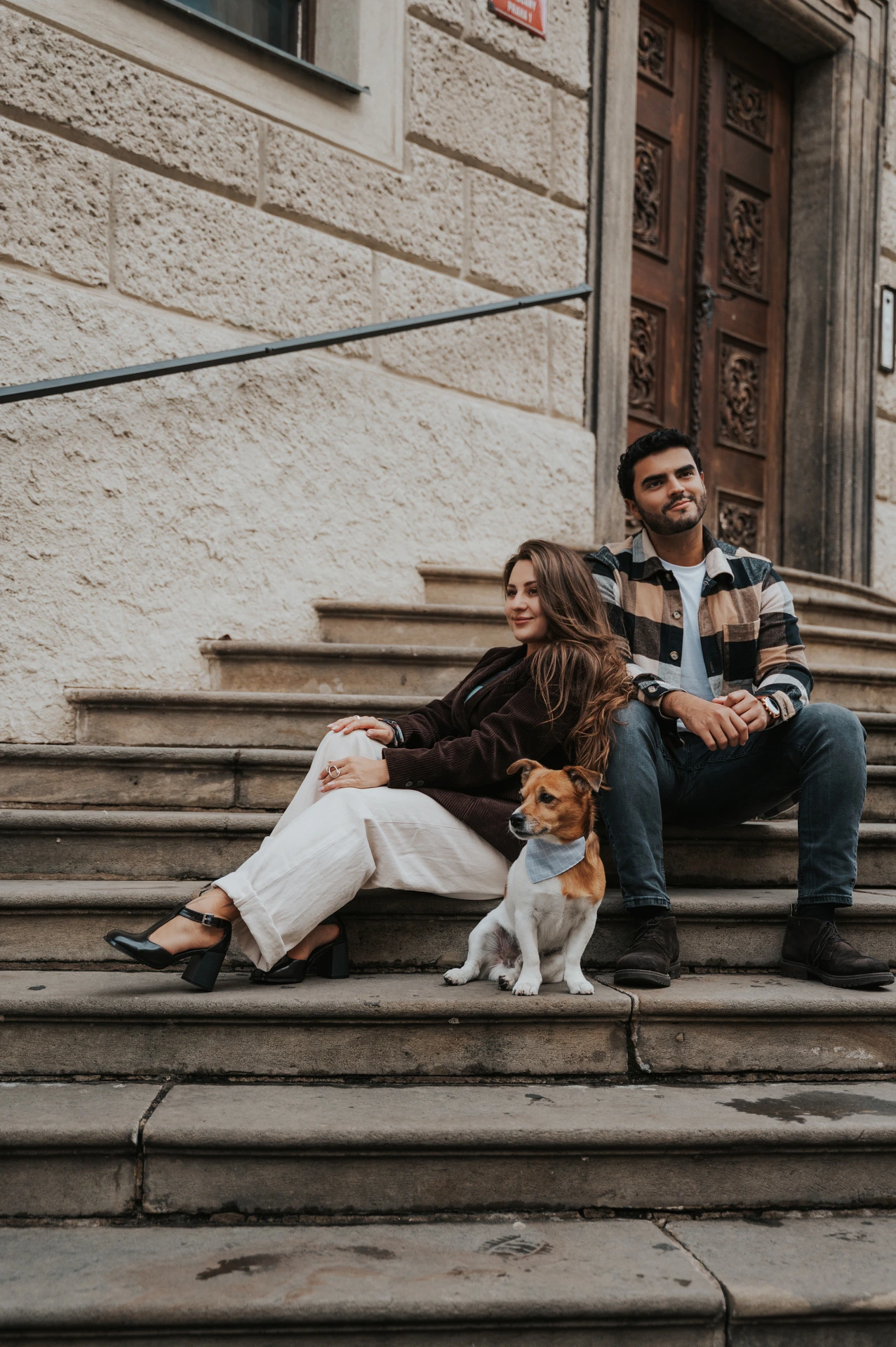 Couple seated together on stone steps with Amigo sitting in front of them during their Prague couple photoshoot.
