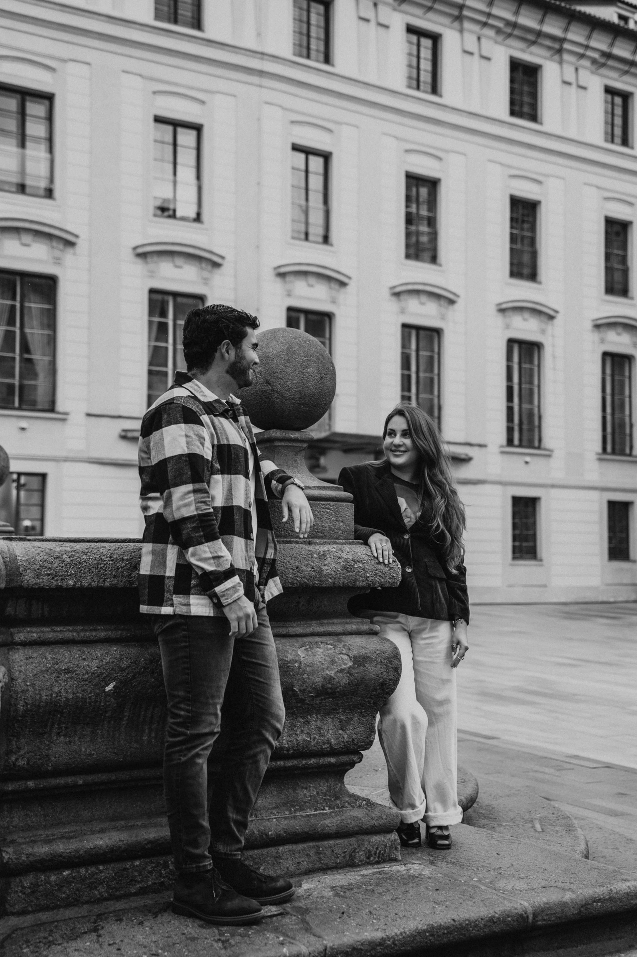Black-and-white portrait of the couple beside a large stone urn in the castle district during their Prague couple photoshoot.