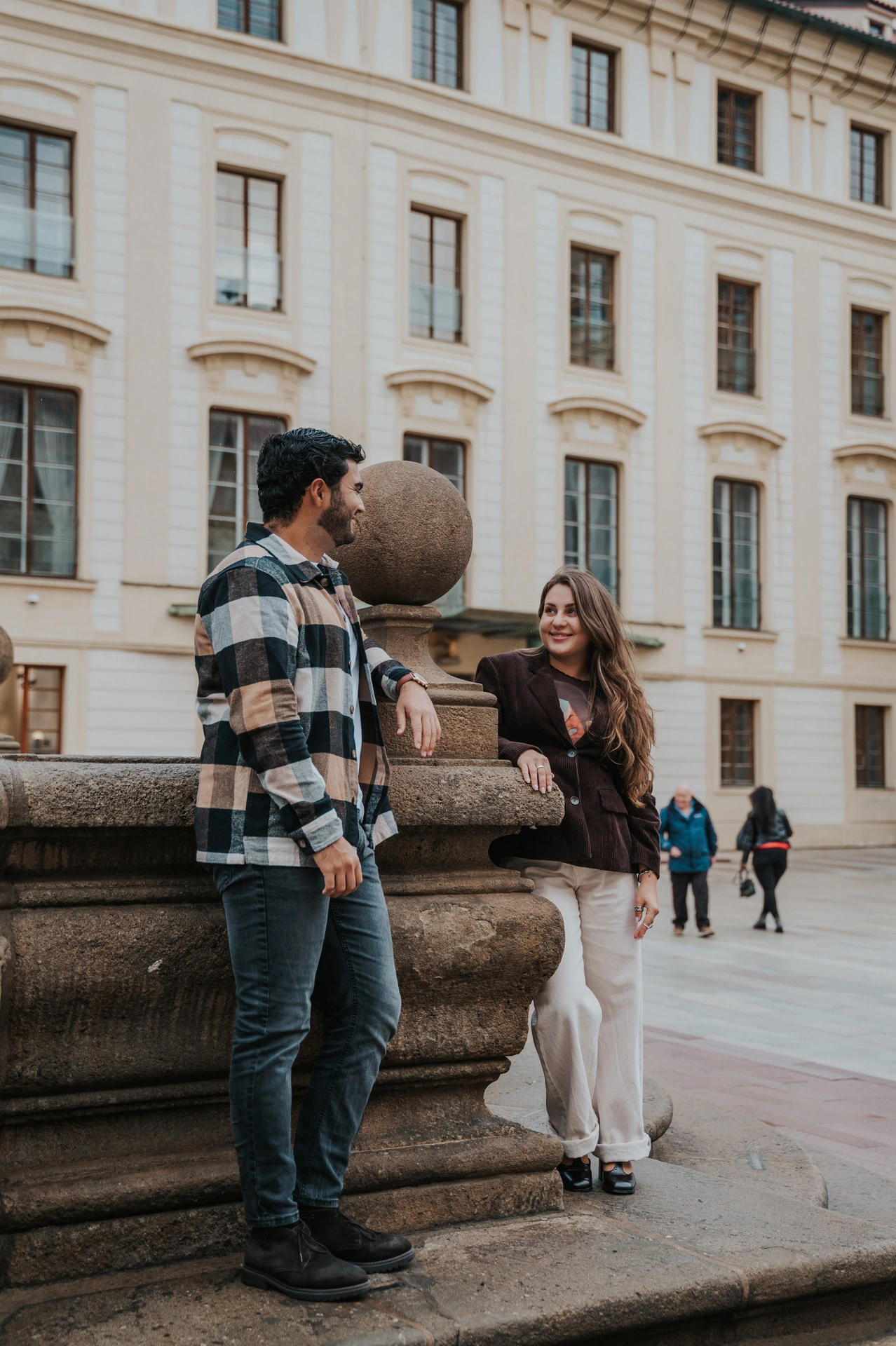 Couple looking at each other beside a large stone urn on the castle square during their Prague couple photoshoot.